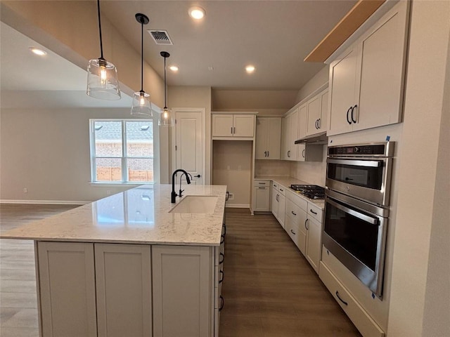 8213 Grenadier Dr, Austin, TX 78738 - kitchen featuring wood finished floors, appliances with stainless steel finishes, under cabinet range hood, white cabinetry, and light stone counters