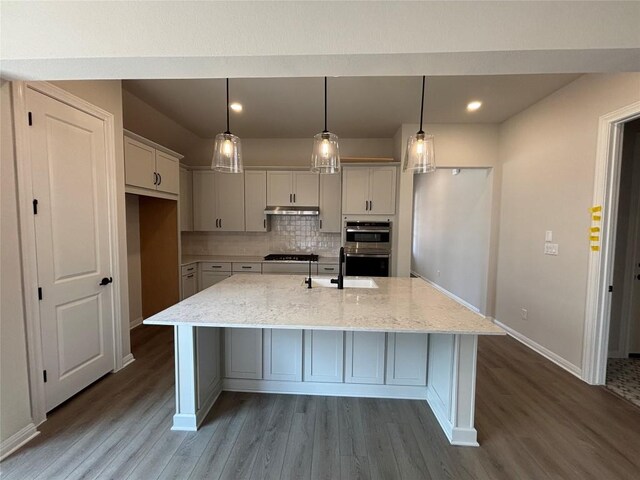 8213 Grenadier Dr, Austin, TX 78738 - kitchen featuring under cabinet range hood, wood finished floors, stainless steel double oven, tasteful backsplash, and light stone counters