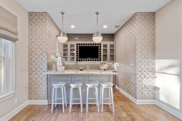2610 Allston Ln, Austin, TX 78746 - kitchen with wood finished floors, a breakfast bar, decorative light fixtures, light countertops, and wallpapered walls