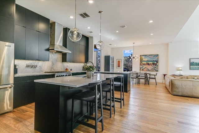 2010 Goodrich Ave Unit 8A, Austin, TX 78704 - kitchen featuring wall chimney range hood, freestanding refrigerator, tasteful backsplash, a kitchen island with sink, and light wood-type flooring