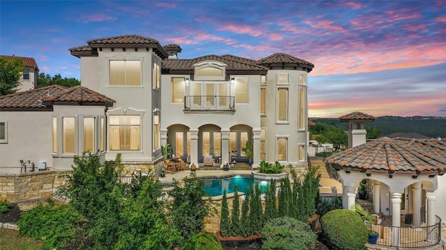 11901 Preserve Vista Ter, Austin, TX 78738 - back of house at dusk with a balcony, a tiled roof, stucco siding, and an outdoor pool
