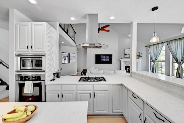 2004 Wood Glen Dr, Round Rock, TX 78681 - kitchen featuring stainless steel appliances, island range hood, a ceiling fan, a fireplace, and white cabinets