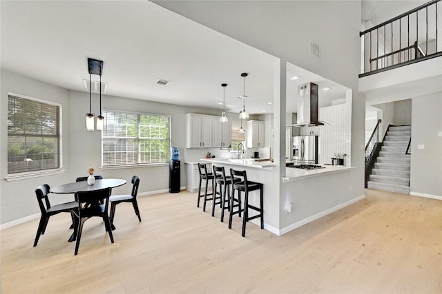 2004 Wood Glen Dr, Round Rock, TX 78681 - kitchen featuring wall chimney exhaust hood, stainless steel appliances, light wood-style floors, a kitchen bar, and light countertops