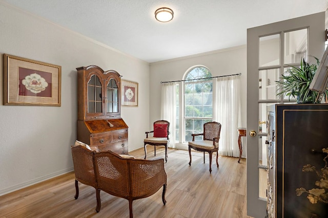 sitting room with light wood-type flooring, ornamental molding, and baseboards