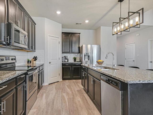 218 Pearland St, Hutto, TX 78634 - kitchen with appliances with stainless steel finishes, a sink, light wood-style floors, a kitchen island with sink, and decorative backsplash