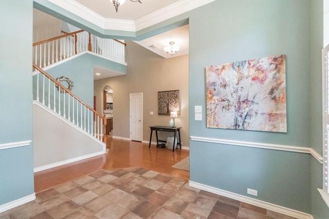 foyer featuring arched walkways, ornamental molding, stairs, baseboards, and a chandelier