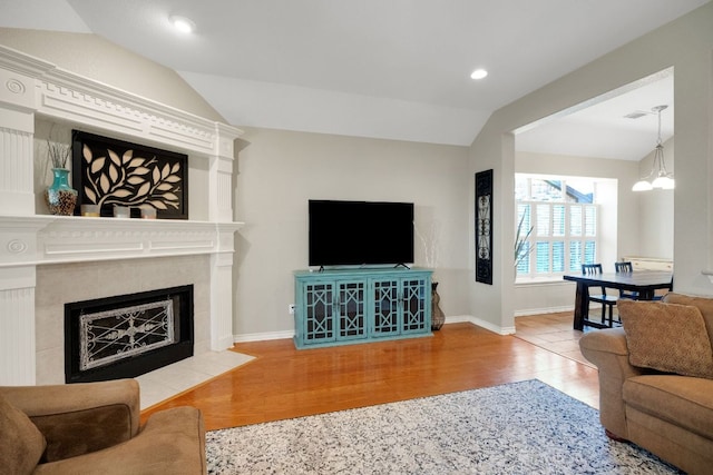 living room featuring lofted ceiling, wood finished floors, a chandelier, baseboards, and a fireplace with flush hearth