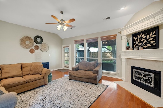 living area featuring vaulted ceiling, a ceiling fan, baseboards, a tile fireplace, and wood finished floors