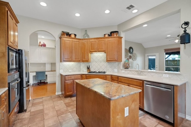 kitchen with appliances with stainless steel finishes, a sink, tasteful backsplash, a center island, and ceiling fan