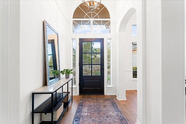foyer entrance with a chandelier, wood finished floors, arched walkways, healthy amount of natural light, and a high ceiling