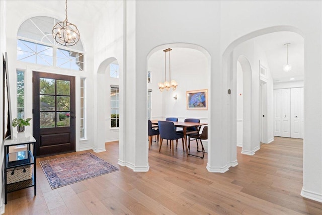 entryway featuring a chandelier, a towering ceiling, light wood-style flooring, baseboards, and arched walkways