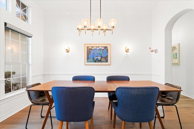 dining room featuring arched walkways, wood finished floors, a chandelier, and baseboards