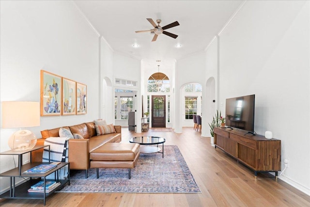 living area featuring crown molding, wood finished floors, a ceiling fan, arched walkways, and a towering ceiling