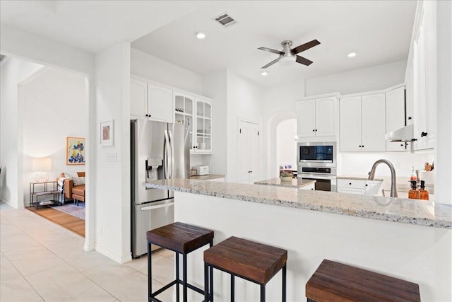 kitchen featuring appliances with stainless steel finishes, a peninsula, a ceiling fan, light stone counters, and arched walkways