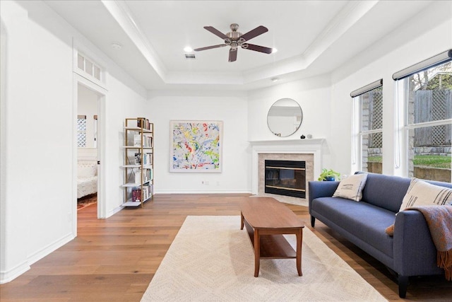 living room with a tray ceiling, ceiling fan, ornamental molding, wood finished floors, and a fireplace with flush hearth