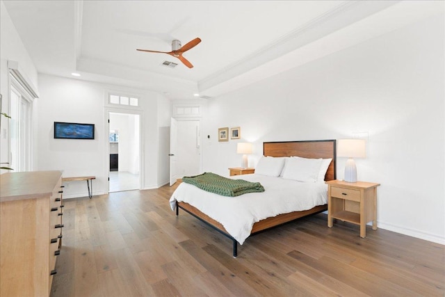 bedroom with a raised ceiling, wood finished floors, recessed lighting, baseboards, and ceiling fan