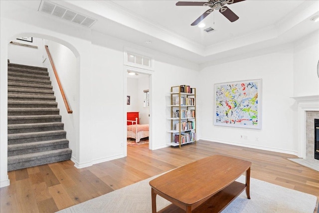 living area featuring wood finished floors, crown molding, ceiling fan, stairs, and a raised ceiling