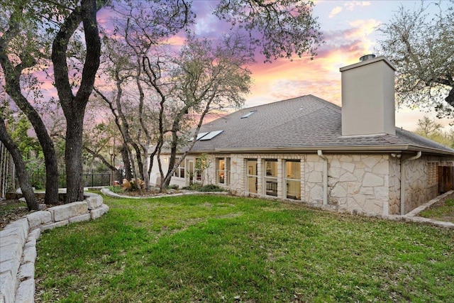 back of house with stone siding, a chimney, and roof with shingles