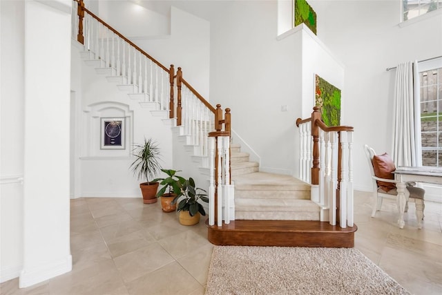 stairs featuring baseboards, a high ceiling, and tile patterned flooring
