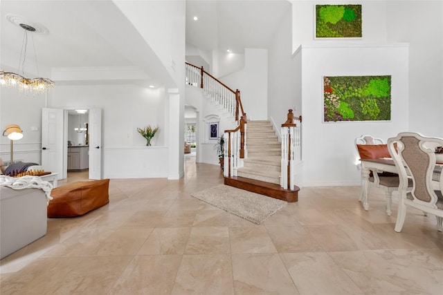 foyer entrance featuring baseboards, a towering ceiling, stairway, and a notable chandelier