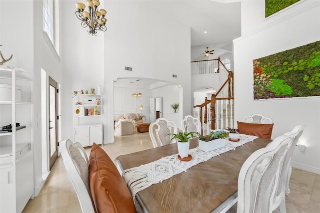 dining room with stairway, ceiling fan with notable chandelier, a towering ceiling, arched walkways, and visible vents
