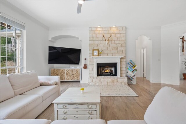 living room featuring crown molding, a ceiling fan, a fireplace, light wood-style flooring, and baseboards
