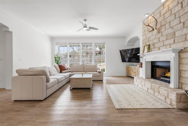 unfurnished living room featuring a large fireplace, crown molding, baseboards, ceiling fan, and wood finished floors