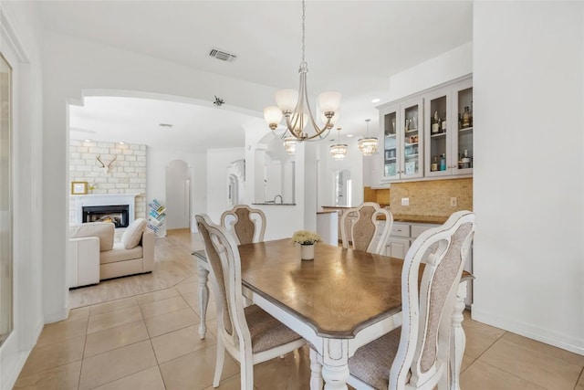 dining room with a notable chandelier, a brick fireplace, light tile patterned floors, visible vents, and arched walkways