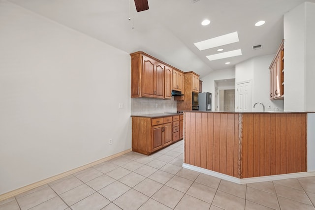 183 Augusta Dr, Wimberley, TX 78676 - kitchen featuring lofted ceiling, stainless steel fridge, a skylight, under cabinet range hood, and tasteful backsplash