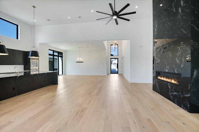 317 Azalea Ct, Horseshoe Bay, TX 78657 - unfurnished living room with a high ceiling, a tiled fireplace, a chandelier, ceiling fan, and light wood-style floors