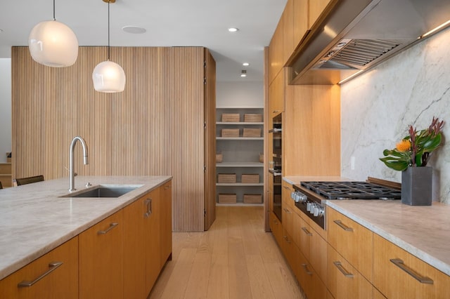 kitchen with a sink, stainless steel gas cooktop, pendant lighting, light wood-style flooring, and range hood