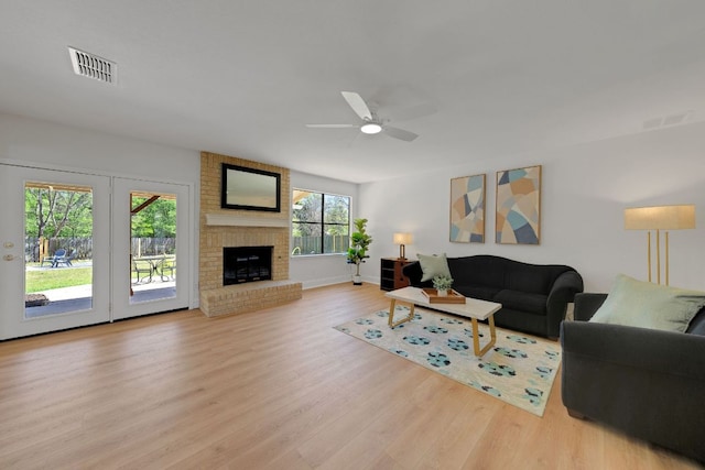 living area featuring baseboards, ceiling fan, visible vents, a fireplace, and wood finished floors