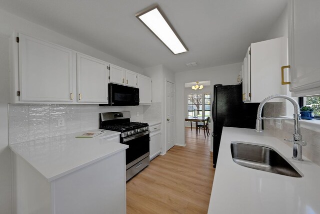 kitchen with white cabinets, light wood finished floors, stainless steel range with gas stovetop, black microwave, and a sink