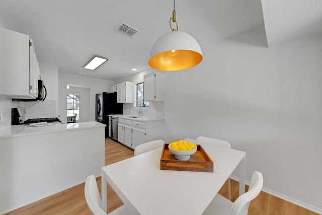 kitchen featuring a sink, a peninsula, visible vents, black appliances, and light wood-style floors