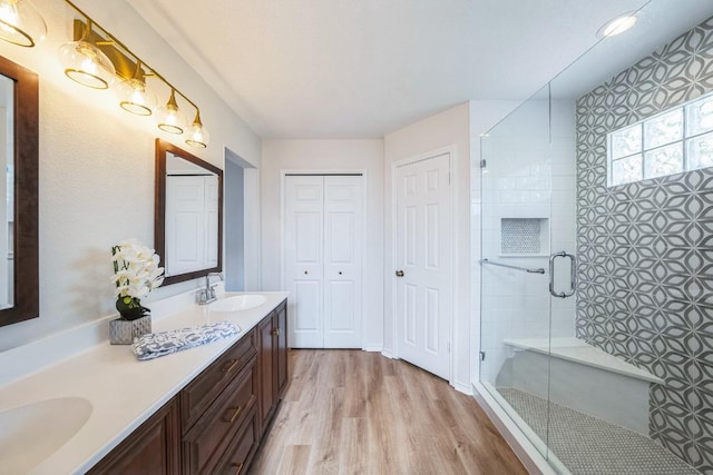 full bathroom with double vanity, a sink, a stall shower, and wood finished floors