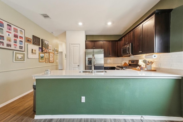 14128 Sandrock Bnd, Pflugerville, TX 78660 - kitchen featuring appliances with stainless steel finishes, a sink, dark brown cabinetry, a peninsula, and tasteful backsplash