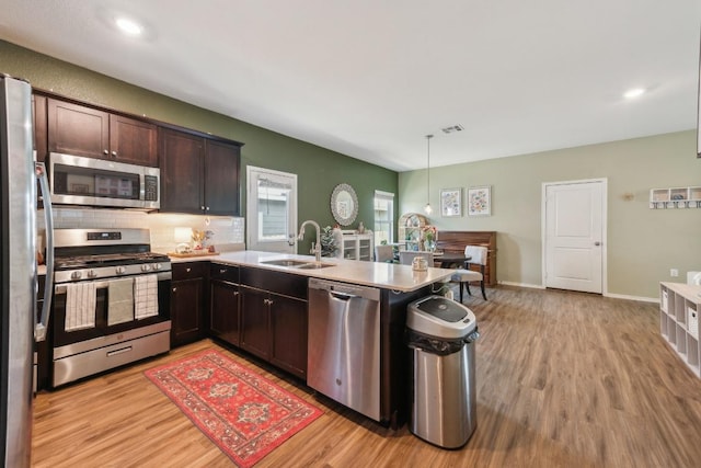 14128 Sandrock Bnd, Pflugerville, TX 78660 - kitchen featuring stainless steel appliances, a sink, light wood-type flooring, a peninsula, and backsplash
