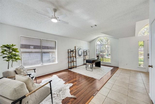 living room with a textured ceiling, lofted ceiling, ceiling fan, and light wood-type flooring
