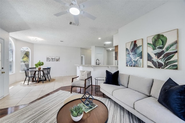 tiled living area with a sink, a textured ceiling, visible vents, and a ceiling fan