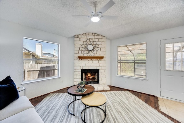 living area with a ceiling fan, lofted ceiling, a fireplace, and a textured ceiling