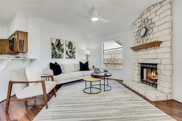 living area with lofted ceiling, a textured ceiling, ceiling fan, a fireplace, and wood finished floors
