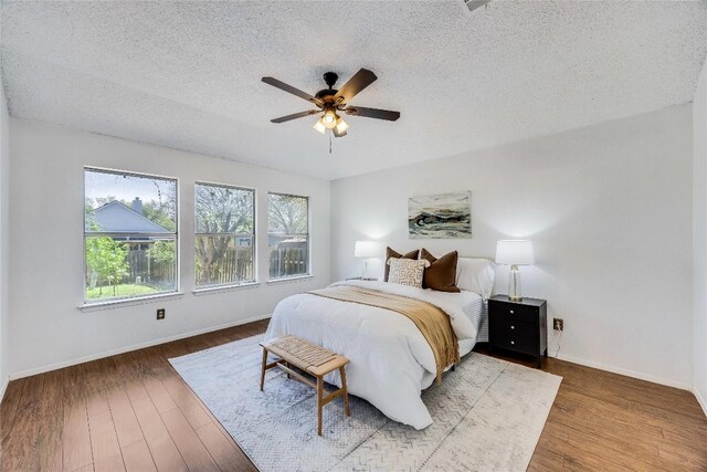 bedroom with baseboards, a textured ceiling, wood finished floors, and a ceiling fan