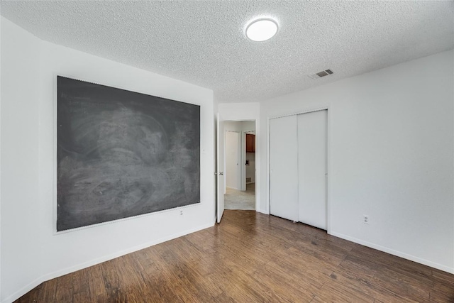 unfurnished bedroom with baseboards, a textured ceiling, visible vents, a closet, and wood finished floors