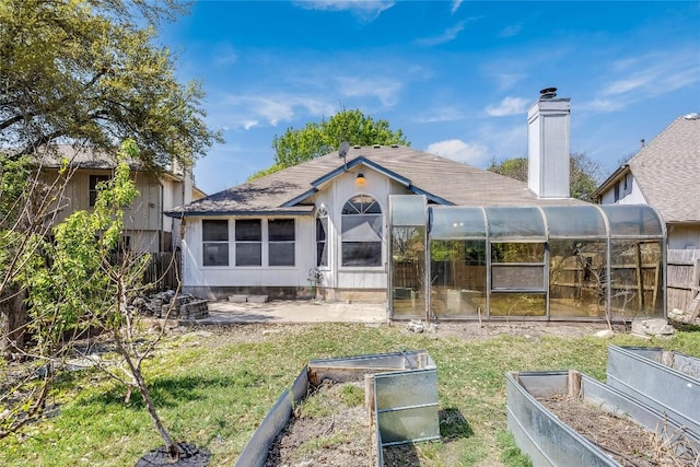 rear view of house with a chimney, a sunroom, a garden, and roof with shingles