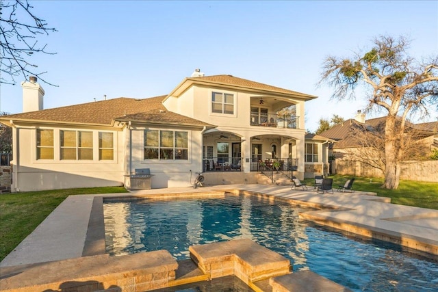 rear view of house with a ceiling fan, a chimney, a balcony, stucco siding, and a patio area