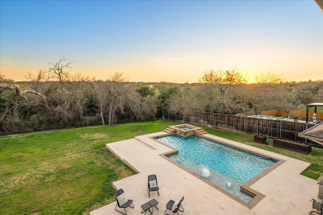 pool at dusk featuring a pool with connected hot tub, a patio area, a lawn, and a fenced backyard