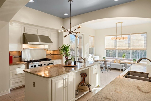 11801 Astoria Dr, Bee Cave, TX 78738 - kitchen featuring under cabinet range hood, a sink, arched walkways, light tile patterned floors, and white cabinets
