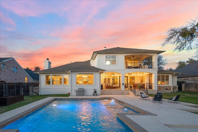 back of property at dusk featuring a ceiling fan, a fenced in pool, a fenced backyard, a balcony, and a patio area