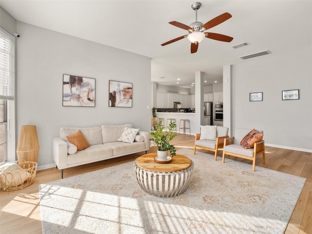 living room featuring light wood-type flooring, baseboards, visible vents, and a ceiling fan