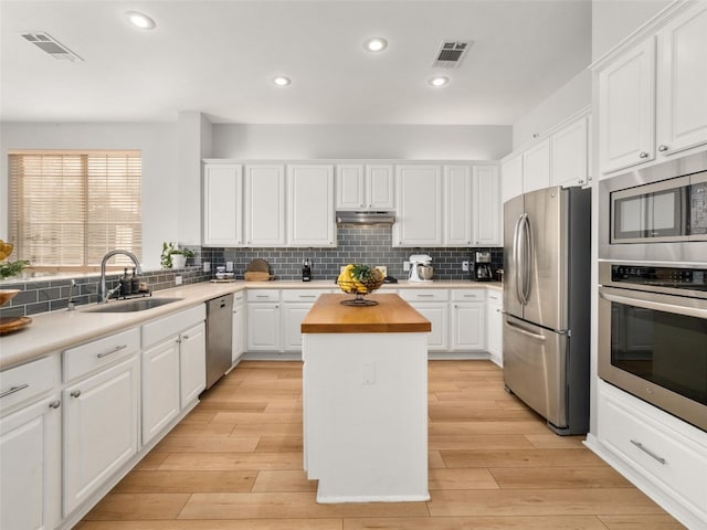 kitchen featuring butcher block countertops, stainless steel appliances, under cabinet range hood, a sink, and visible vents